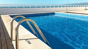 A clear blue pool with metal ladders, a lifeguard stand, and a view of the ocean. - Charming Flat With Amazing sea Line View (Cascais)