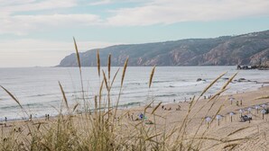 A beach with people, umbrellas, and a rocky cliff in the background. - Charming Flat With Amazing sea Line View (Cascais)