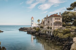 A coastal building with a lighthouse, rocky shoreline, and calm sea. - Charming Flat With Amazing sea Line View (Cascais)