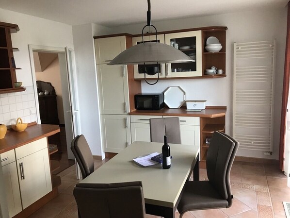 A kitchen with a dining table, chairs, a microwave, a wine bottle, and cabinets.