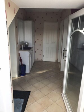 A narrow hallway with a kitchen area on the left, a white door at the end, and a glass door on the right.