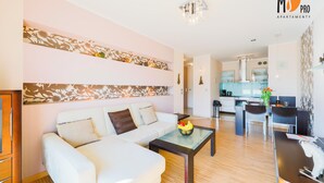 A modern living room with a white sofa, a glass coffee table, and a kitchen area in the background. - MS Pro Apartamenty AQUARIUS (Kolobrzeg)