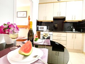 A modern kitchen with white cabinets, a microwave, and a sink. There is a dining table with a plate of watermelon and two glasses of wine. - Adeje House, 2 bedrooms Wifi Free (Adeje)