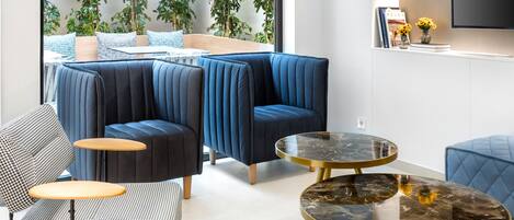 Una sala de estar moderna con un sofá, sillones y una mesita de centro. Se ve un ventanal con plantas afuera.