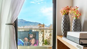 Una habitación con vista a un paisaje urbano, una ventana con cortinas y dos jarrones en un estante de madera.