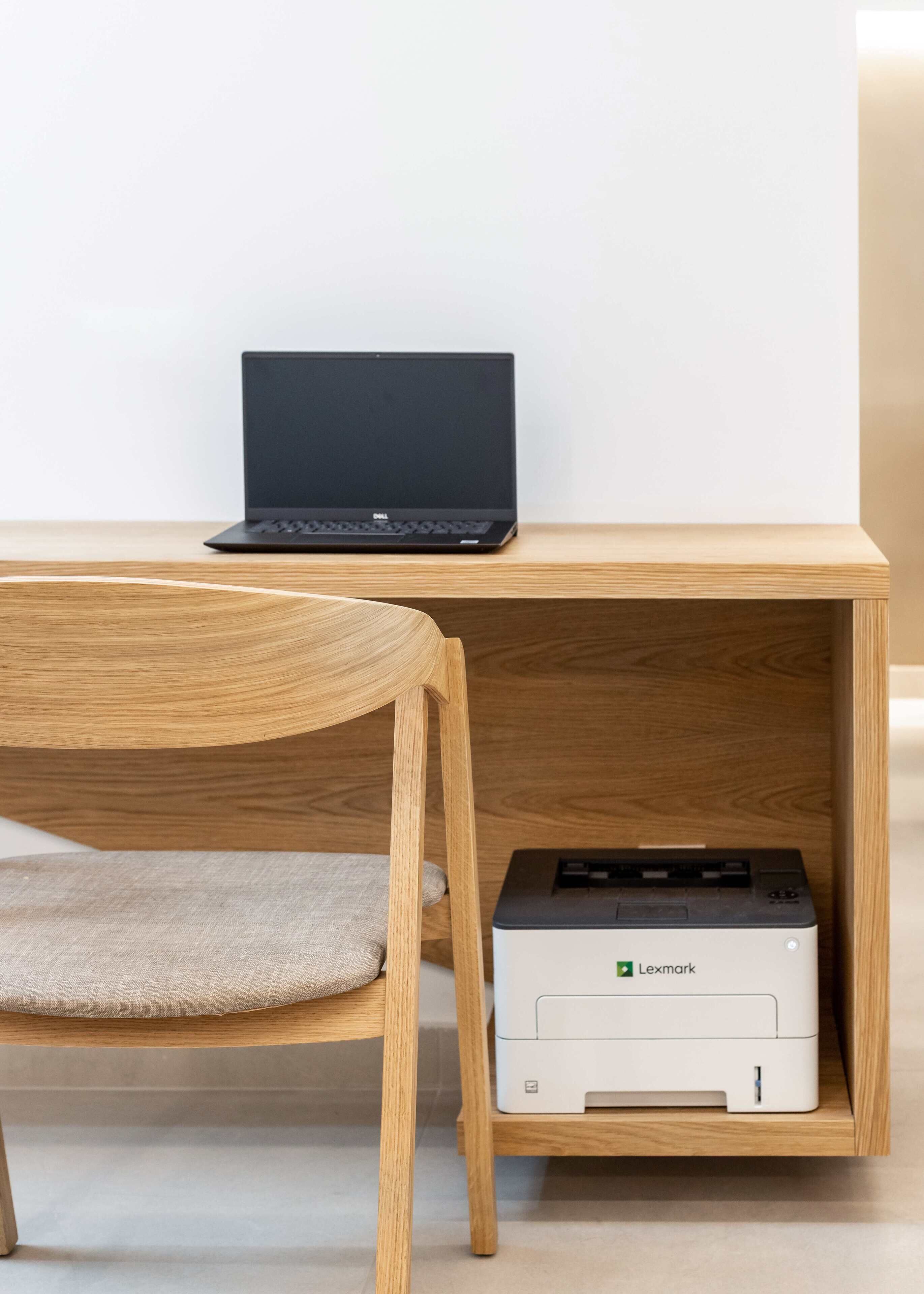 Una computadora portátil sobre un escritorio de madera con una impresora Lexmark debajo.