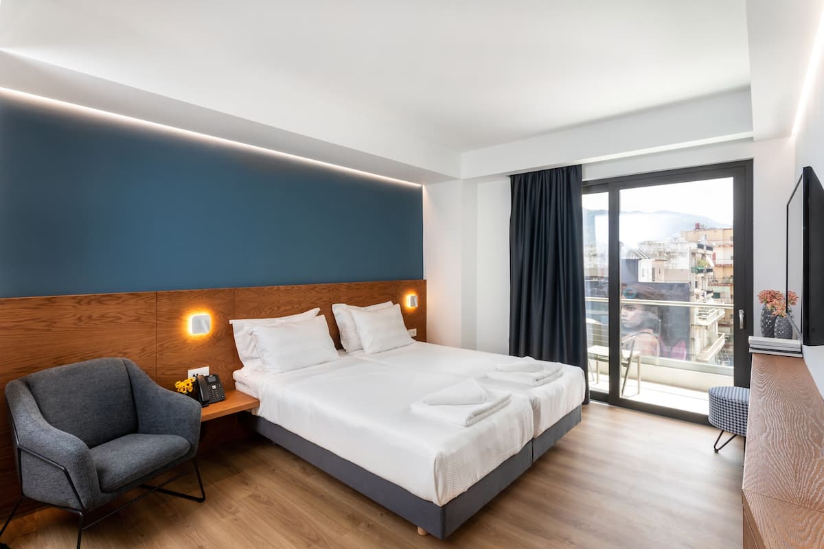 Habitación de hotel moderna con una cama grande, zona de estar, cabecera de madera y vistas a la ciudad.
