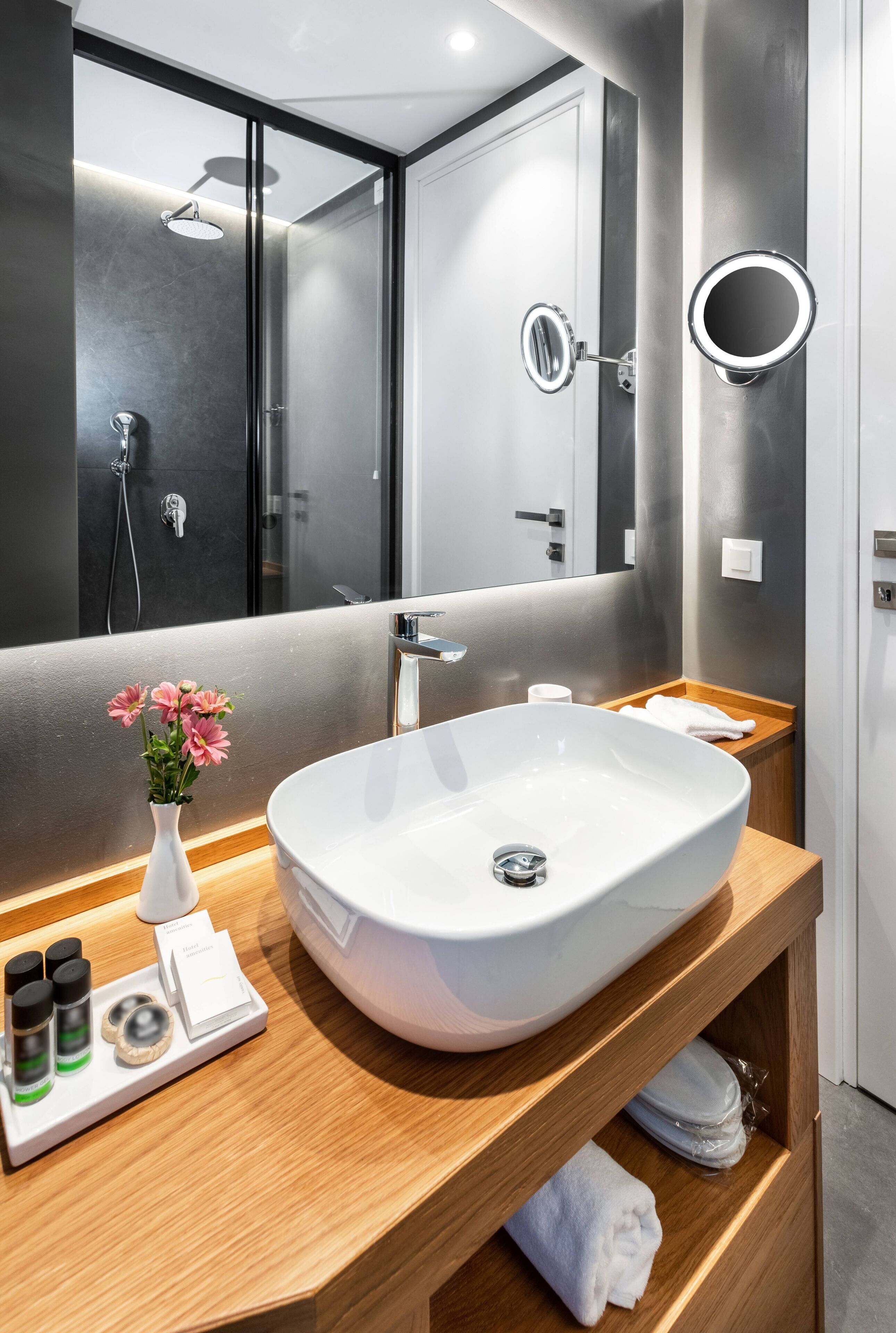 Un bagno moderno con un ampio lavandino bianco, uno specchio e una doccia.
