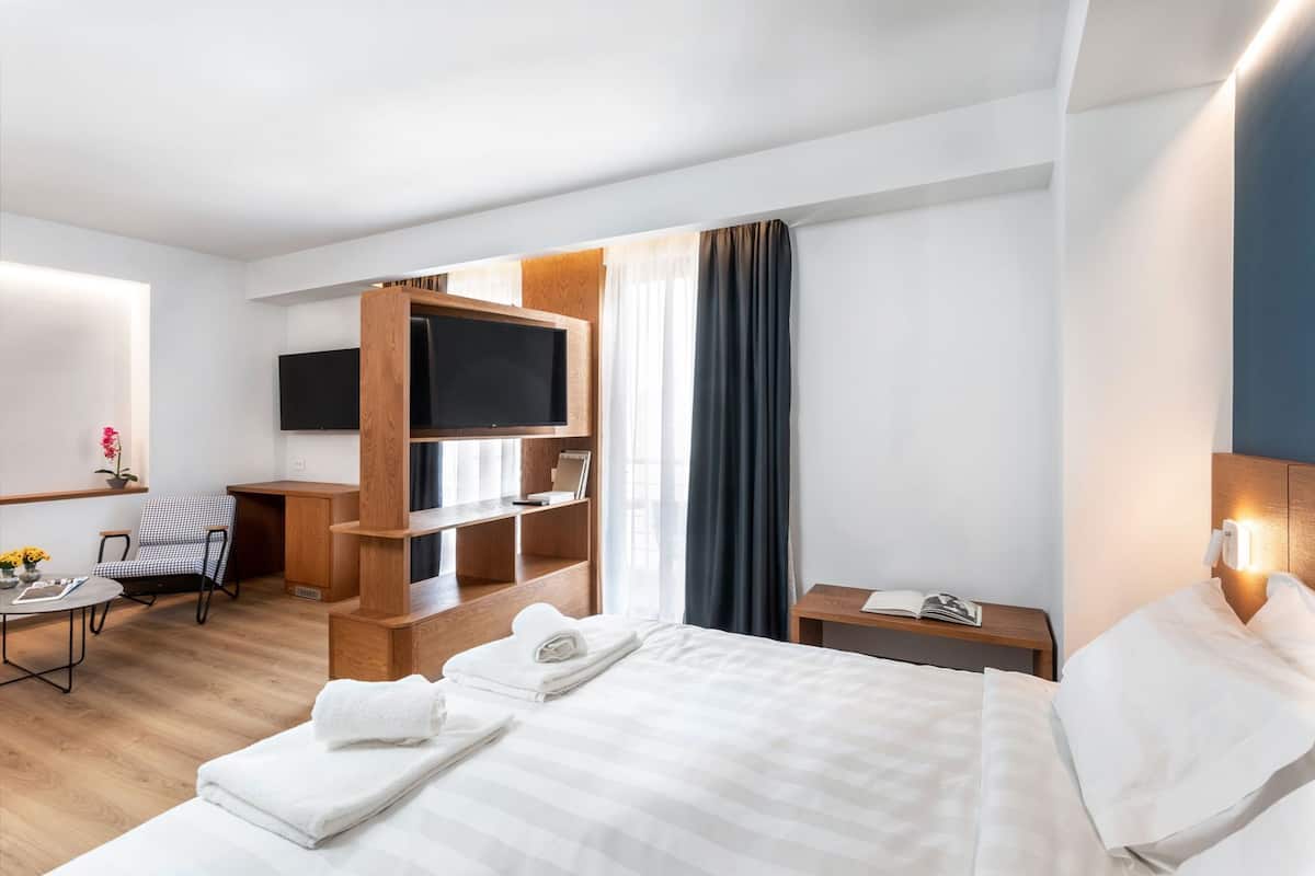 Habitación de hotel con cama, escritorio, silla, televisión, mesita de noche y ventana con cortinas.