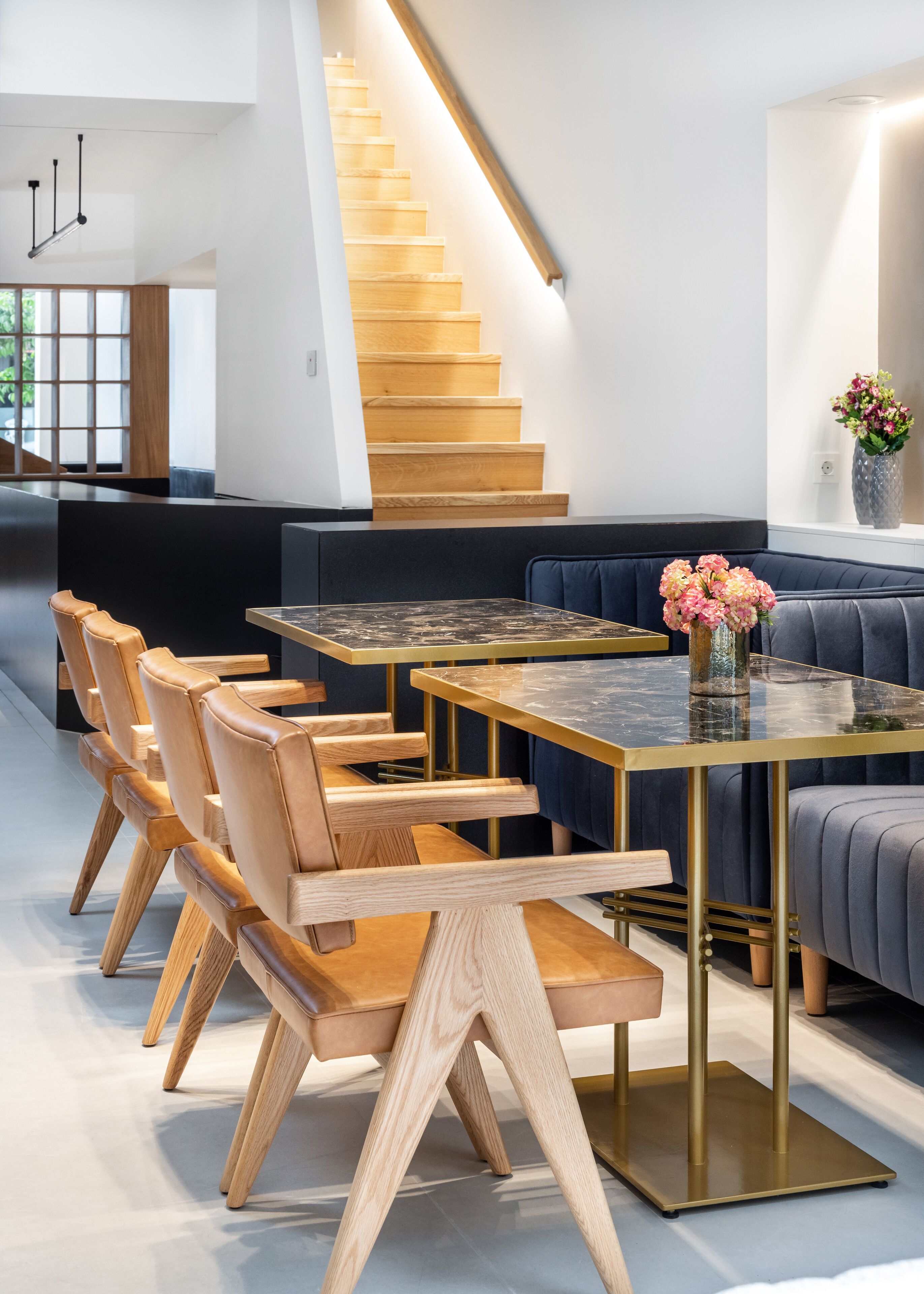 A modern interior with a wooden staircase, a dining area with a glass-top table and wooden chairs, and a blue sofa.