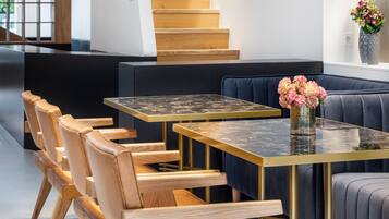 Un interior moderno con una escalera de madera, un comedor con una mesa de vidrio y sillas de madera, y un sofá azul.
