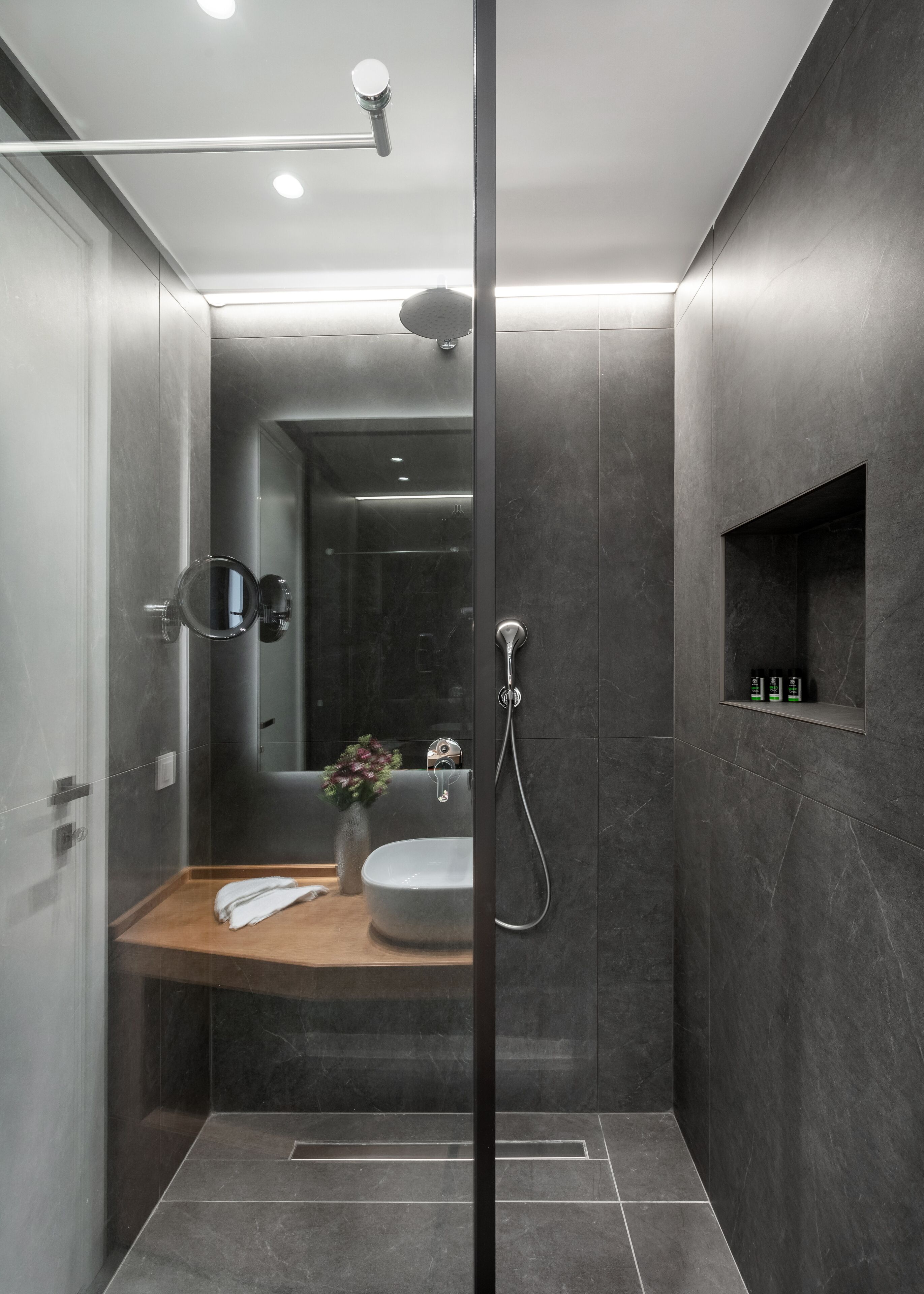 Un baño moderno con cabina de ducha de vidrio, tocador de madera, lavamanos y espejo.