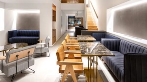Un interior moderno con una zona de estar central, mesas de madera y una escalera.