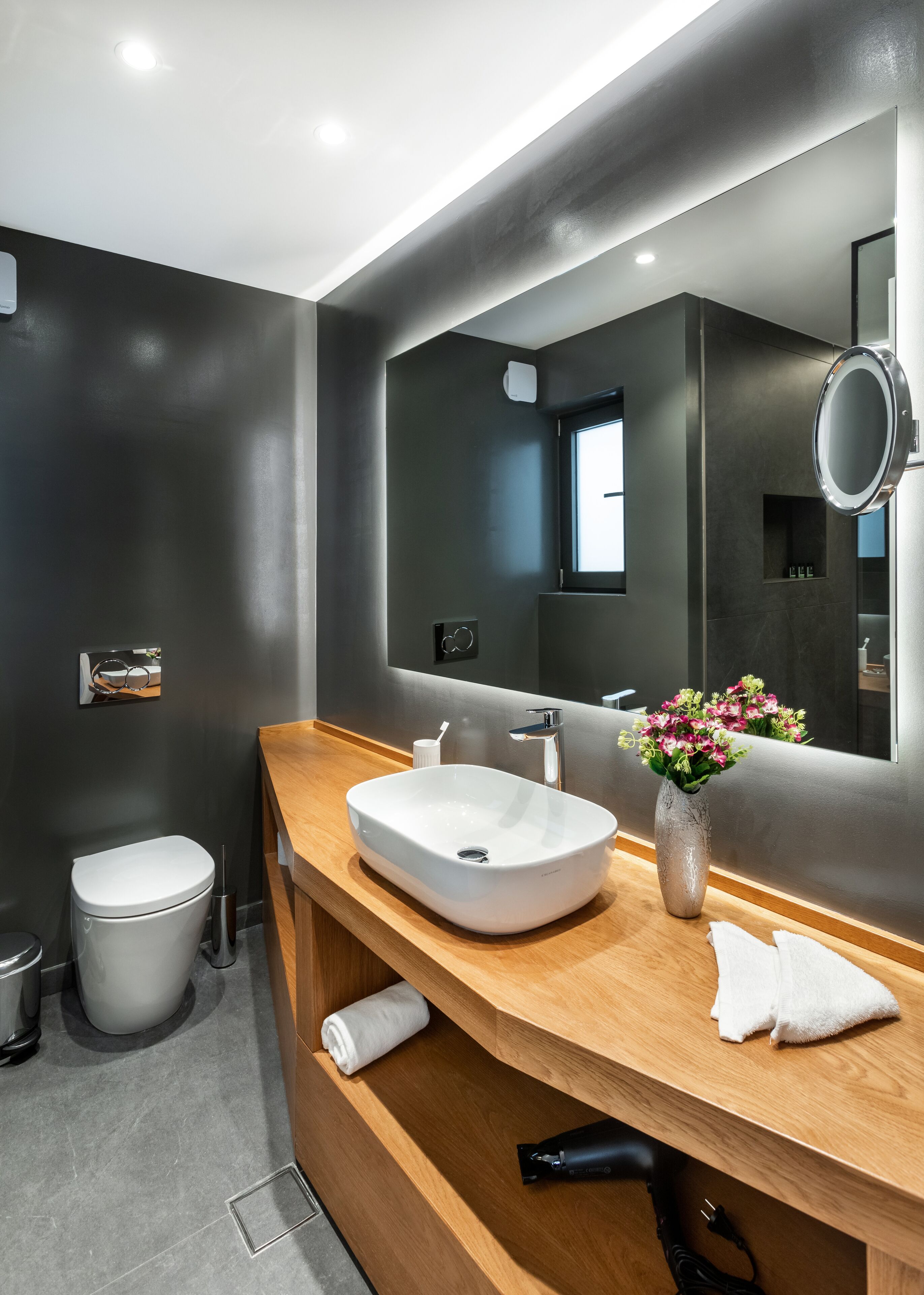 A modern bathroom with a large mirror, a white sink, and a wooden vanity.