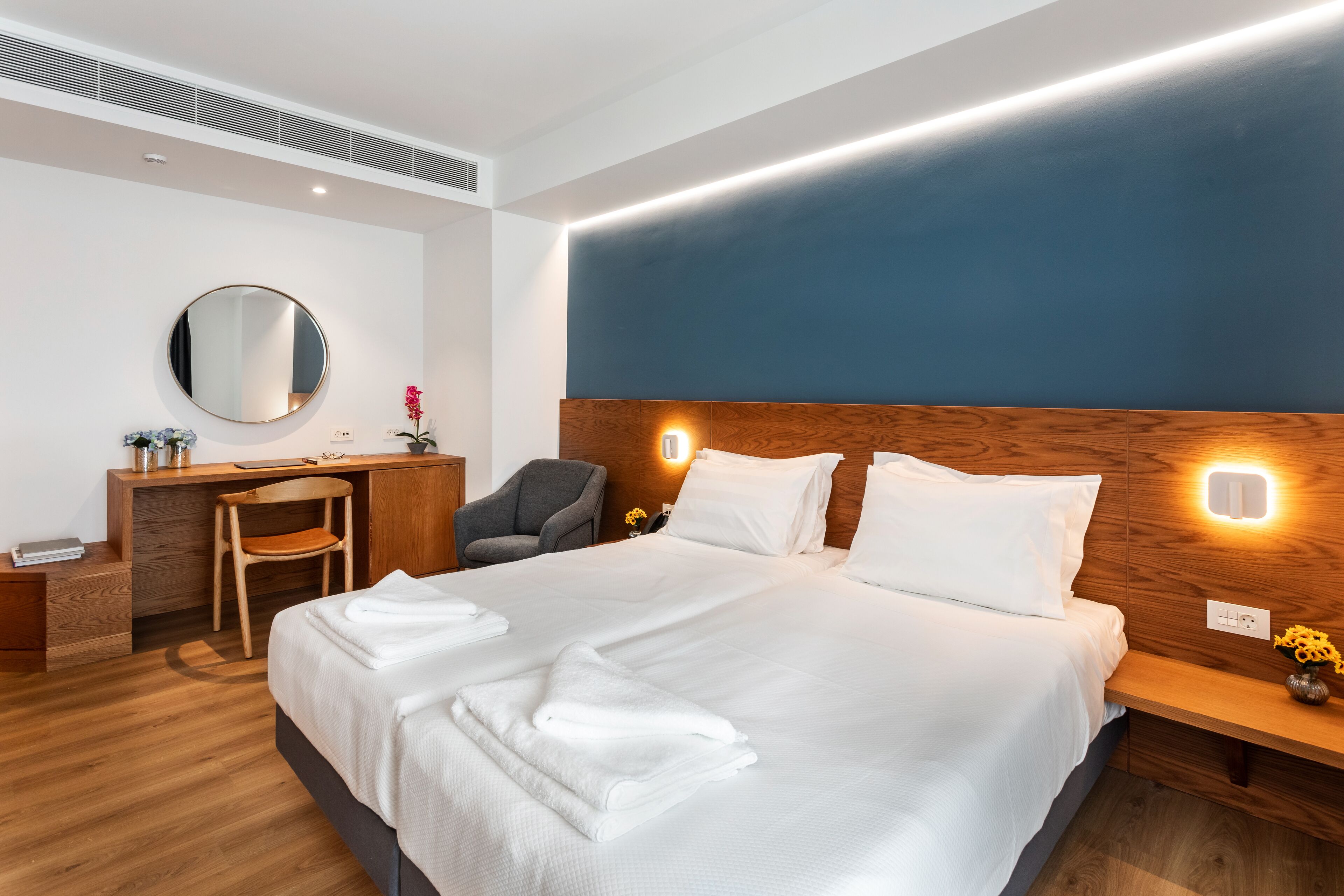 Una habitación de hotel moderna con una cama grande, cabecero de madera, mesitas de noche, un escritorio y una silla.