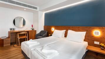 A modern hotel room with a large bed, wooden headboard, bedside tables, a desk, and a chair.