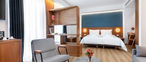 A modern hotel room with a large bed, a desk, a chair, and a sofa.