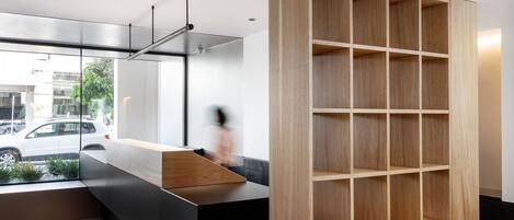 Un área de recepción moderna con una estantería de madera, una barra de mostrador negra y vistas a la calle.