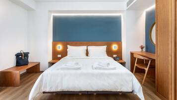 Een moderne hotelkamer met een groot bed, een houten hoofdbord, nachtkastjes, een bankje, een bureau en een spiegel.