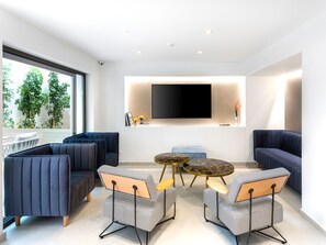 Ein modernes Wohnzimmer mit Flachbildfernseher, bequemen Sitzmöglichkeiten und Blick ins Grüne.