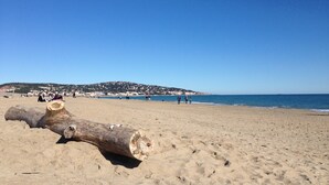 A sandy beach with a large log in the foreground and a distant view of a town across the water. - Lovely 1BR with garage near beach in Sète, pets allowed (Sète)