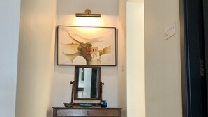 A hallway with a wall-mounted light fixture, a framed painting, a mirror, and a small table with decorative items.