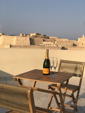 A table with a bottle of champagne and two glasses on a balcony overlooking a fortified city. - Gran Harbour Penthouse (L-Isla)