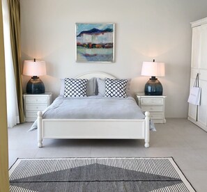 Une chambre à coucher bien rangée, avec un lit, deux tables de chevet avec des lampes, un tableau au mur et une armoire.