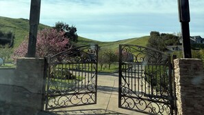 A gated entrance with a pergola structure, a clear sky, and a hilly landscape with blooming trees. - Powell Ranch-Pool & Jacuzzi on Beautiful Farm (Exeter)