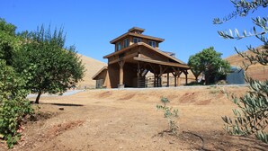 A two-story wooden house with a balcony, surrounded by dry, sandy terrain and sparse vegetation. - Powell Ranch-Pool & Jacuzzi on Beautiful Farm (Exeter)