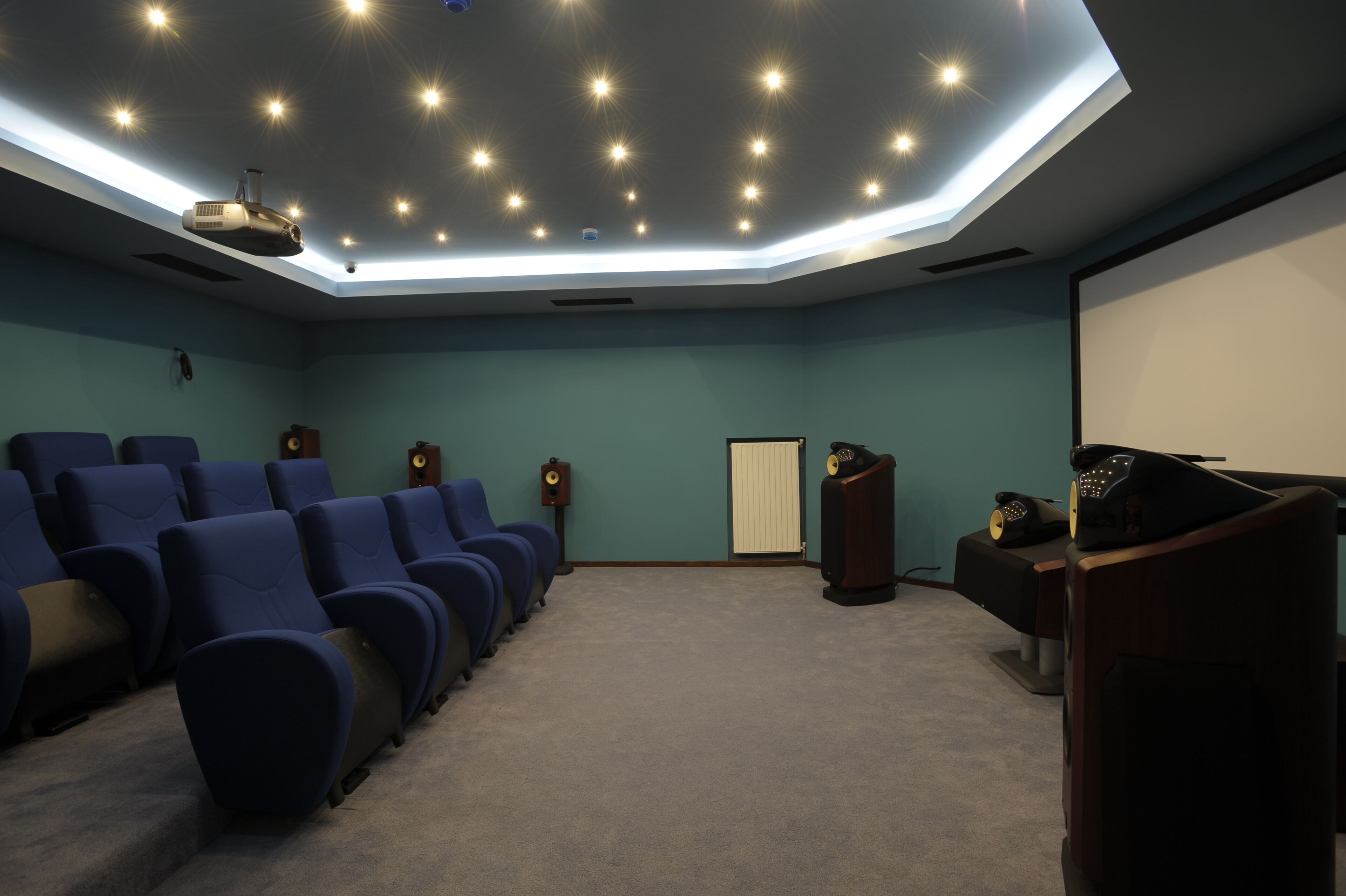 Un cine con hileras de asientos azules, una pantalla grande, un proyector en el techo y un atril de madera.