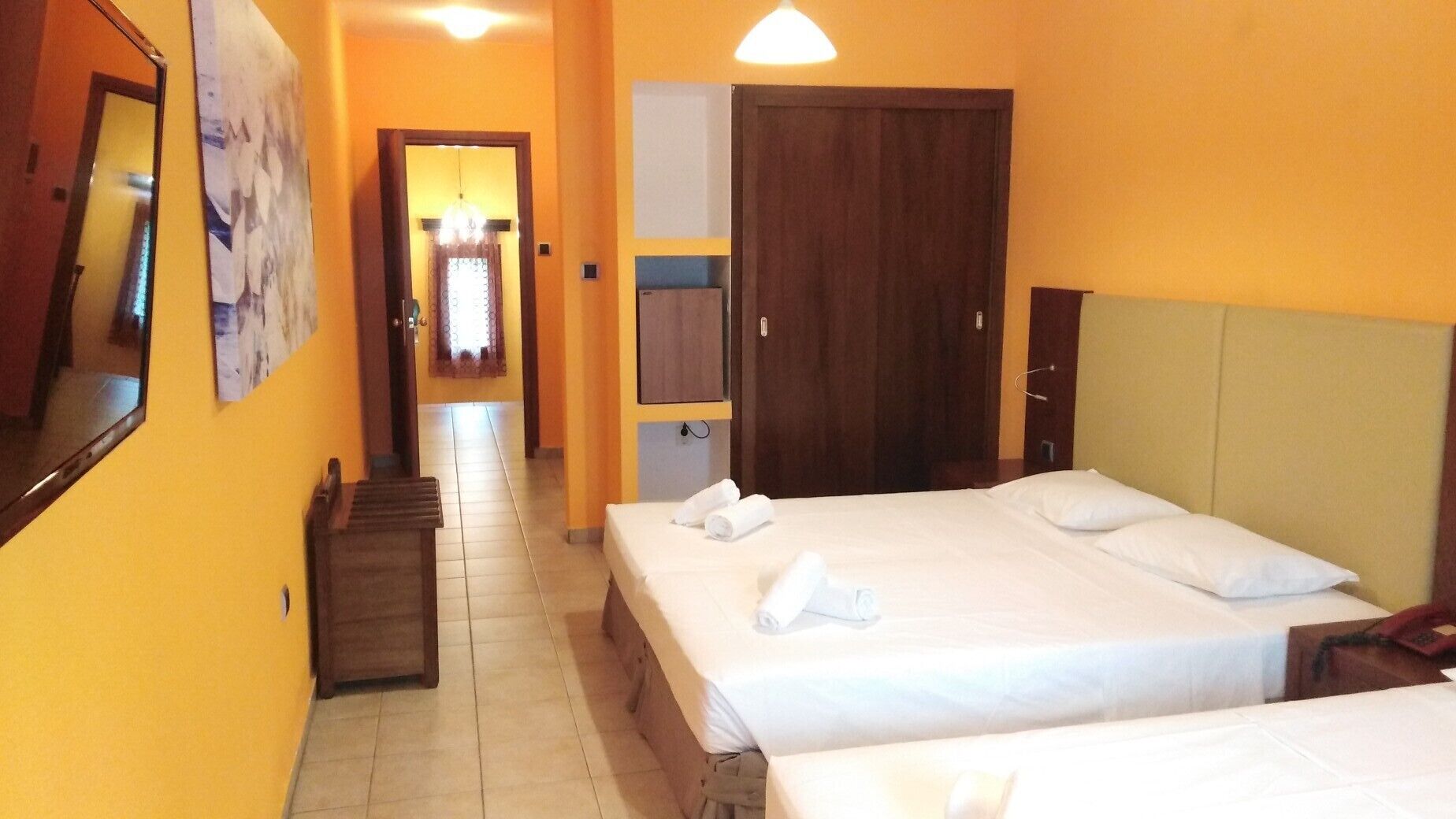 A hotel room with two beds, a wooden headboard, a wardrobe, and a mirror on the wall.