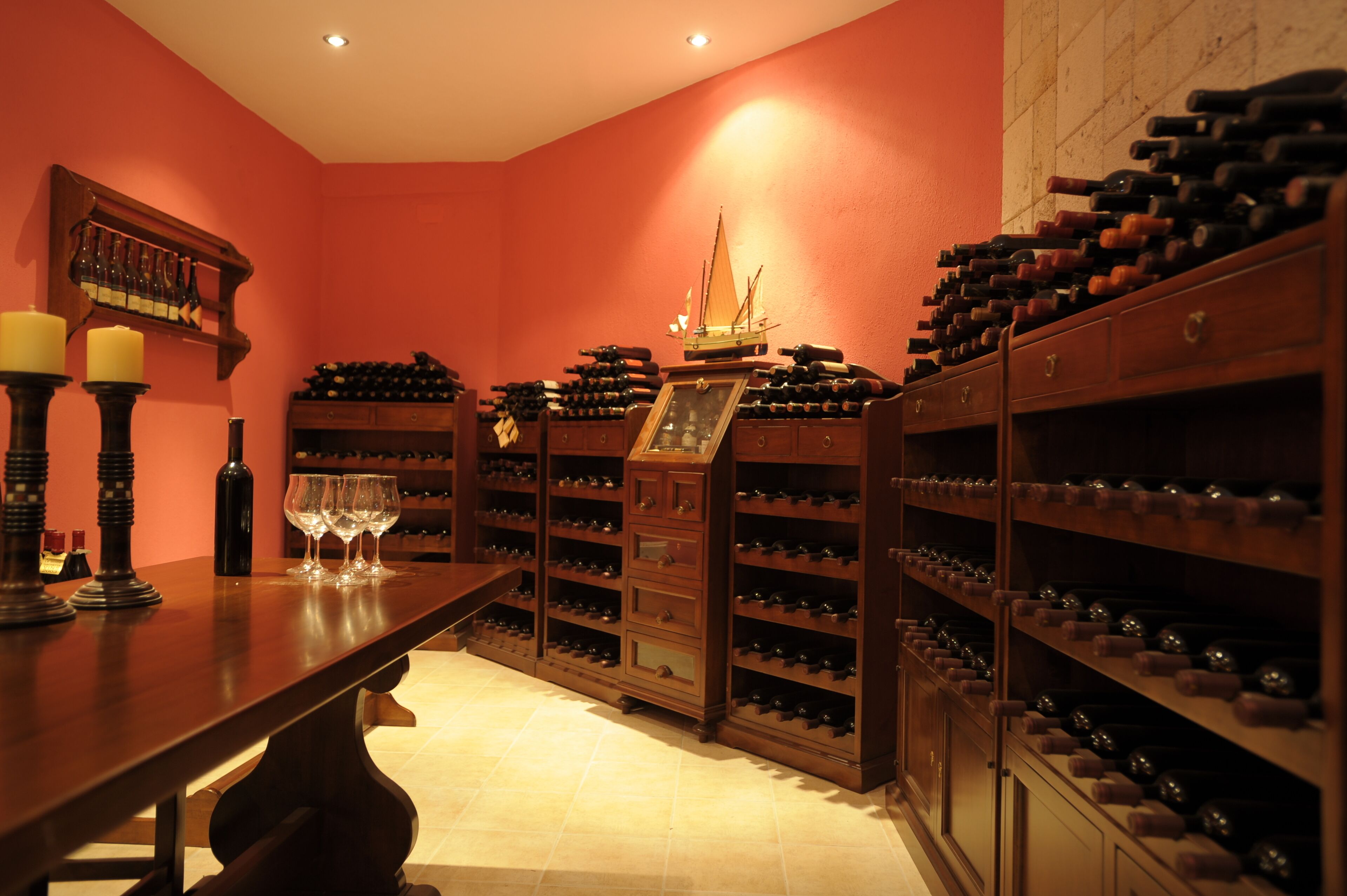 A wine cellar with wooden racks of wine bottles, a ship model, and wine glasses on a table.