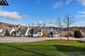 A row of white houses with grey roofs and chimneys, set against a backdrop of hills and a clear blue sky.