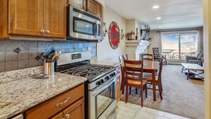 Una cocina con armarios de madera, una estufa de acero inoxidable y un microondas. Hay una zona de comedor con una mesa y sillas.