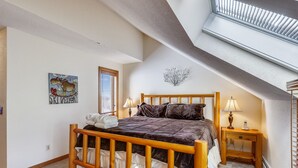 Un dormitorio con cama de madera, una mesita de noche con lámpara, una ventana con persianas y un adorno en la pared.