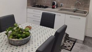 A compact kitchen with a gas stove, a sink, and white cabinets. There is a table with a patterned tablecloth and a basket of limes. - La Casa del Corso (Avola)