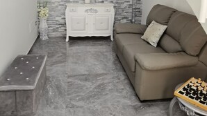 A modern living room with a grey marble floor, a white console table with a vase of flowers, a beige sofa, and a chess table. - La Casa del Corso (Avola)
