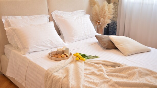 Una cama bien hecha con ropa blanca, un plato de galletas y un ramo de flores amarillas.