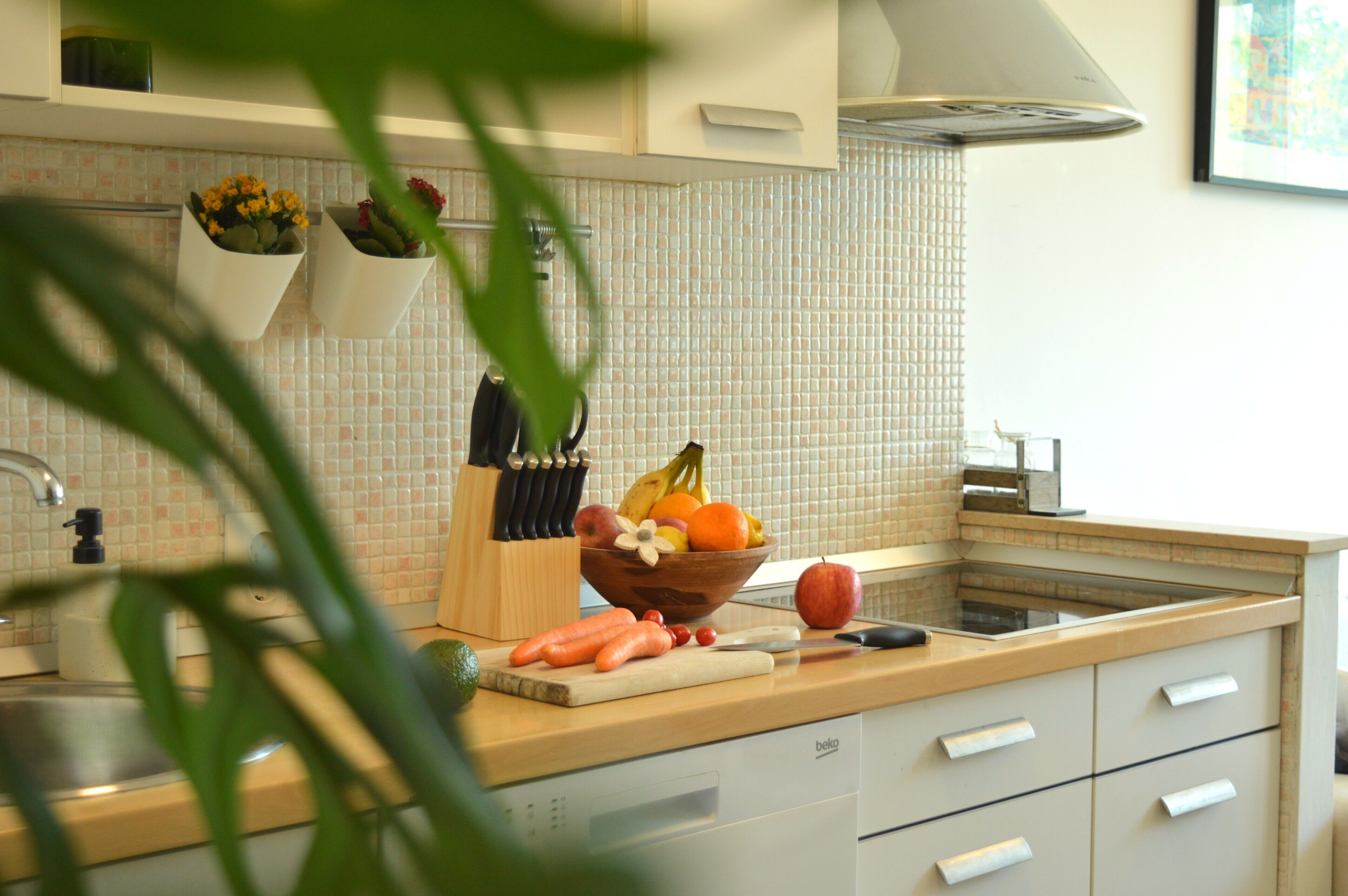 A kitchen with a tiled backsplash, a fruit bowl, a cutting board with vegetables, and a dishwasher.