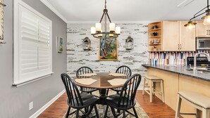 A dining area with a round table, black chairs, a chandelier, and a kitchen with wooden cabinets and a countertop. - Adorable 3 bed, 2 bath Cottage in Glynn Haven SD (Saint Simons Island)