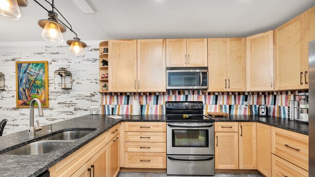 A modern kitchen with wooden cabinets, stainless steel appliances, a striped backsplash, and pendant lighting. - Adorable 3 bed, 2 bath Cottage in Glynn Haven SD (Saint Simons Island)
