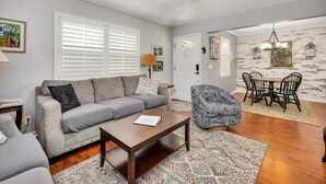 A living room with a sofa, coffee table, patterned rug, and a dining area with a table and chairs. - Adorable 3 bed, 2 bath Cottage in Glynn Haven SD (Saint Simons Island)