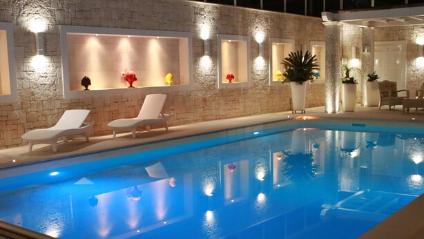 A swimming pool with lounge chairs and wall-mounted lights.