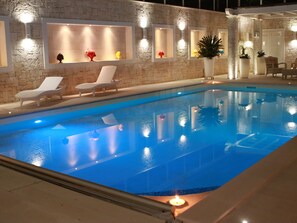 A swimming pool with lounge chairs and wall-mounted lights. - Villa Caraitria by Pugliadamare (Martina Franca)