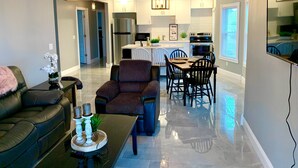 A modern living room with a sofa, coffee table, and a dining area with chairs and a table. - The Maid of the Mist Villa-Yard &Parking (Niagara Falls)