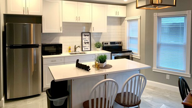 A modern kitchen with white cabinets, stainless steel appliances, and a central island with seating. - The Maid of the Mist Villa-Yard &Parking (Niagara Falls)
