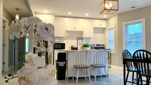 A modern kitchen with white cabinets, a central island, and a dining area with white chairs. - The Maid of the Mist Villa-Yard &Parking (Niagara Falls)