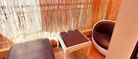A room with a bamboo wall, a small table, two cushioned seating areas, and a tiled floor.