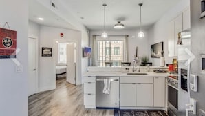Una cocina moderna con armarios blancos, una isla central, iluminación colgante y vistas a un edificio.